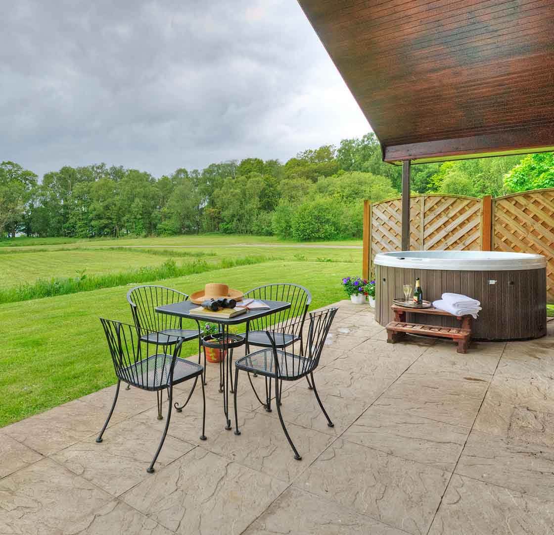 Outside patio with table, chairs and a hot tub with a view over Loch Lomond at a Chalet at Loch Lomond Waterfront