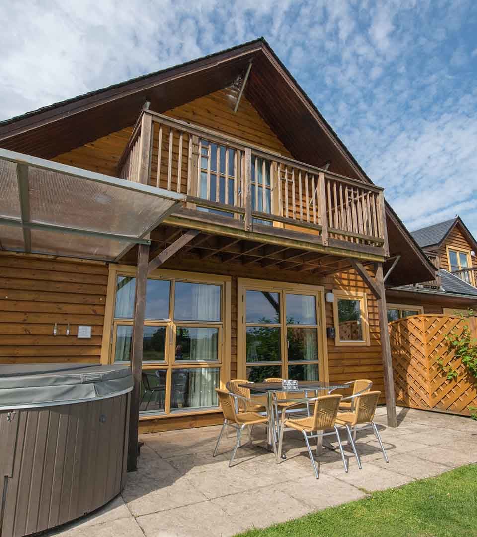 An exterior view of a Diamond Lodge with and outside seating area and hot tub at Loch Lomond Waterfront