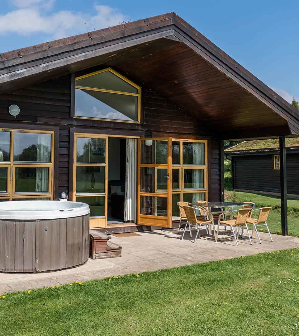 The exterior of the Drummond / Honeymoon Suite chalet at Loch Lomond Waterfront in Balmaha with a hot tub outside