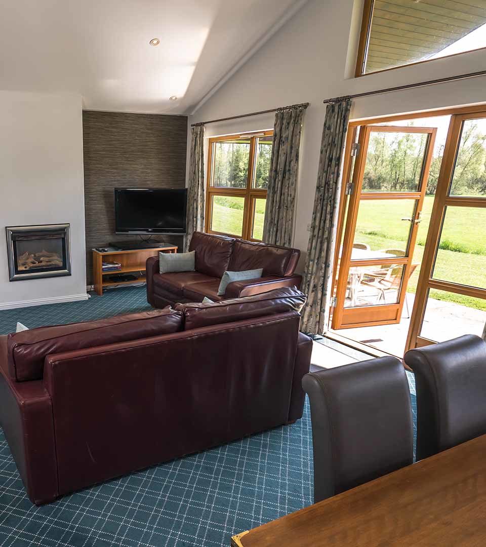 The living area with patio doors opening to the patio in the Drummond / Honeymoon Suite chalet at Loch Lomond Waterfront in Balmaha