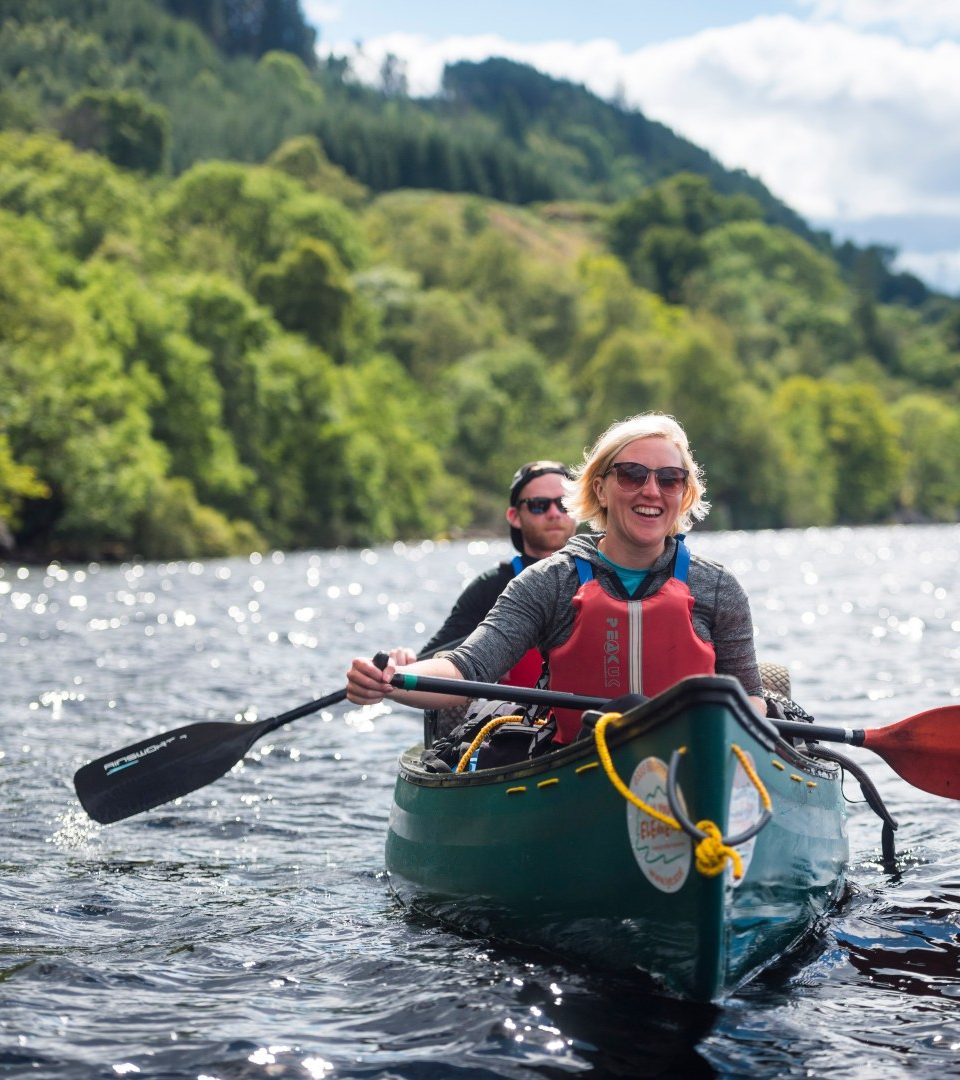 A man and a lady canoeing Loch Lomond on a bright summers day with In Your Element on a Canoe Safary