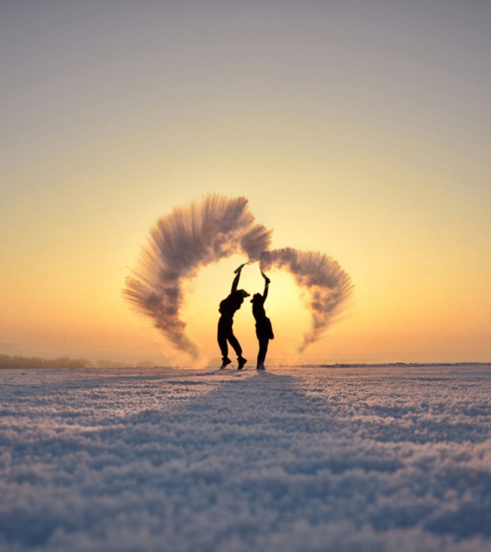 Romantic couple throwing champagne in snow to make a love heart above them