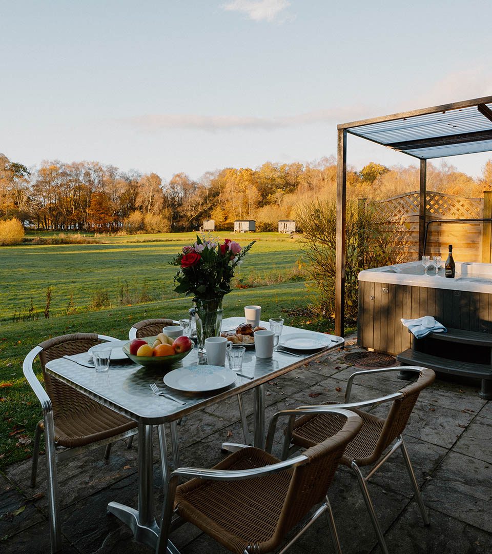 Outside dining table and hot tub on the patio at a Diamond Lodge at Loch Lomond Waterfront luxury lodges in Balmaha