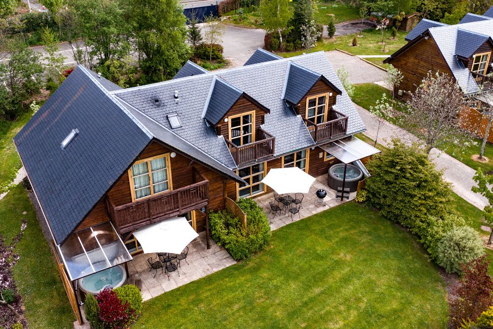 Loch Lomond Waterfront Lodges Aerial view looking down on lodge and lawn with hot tub.