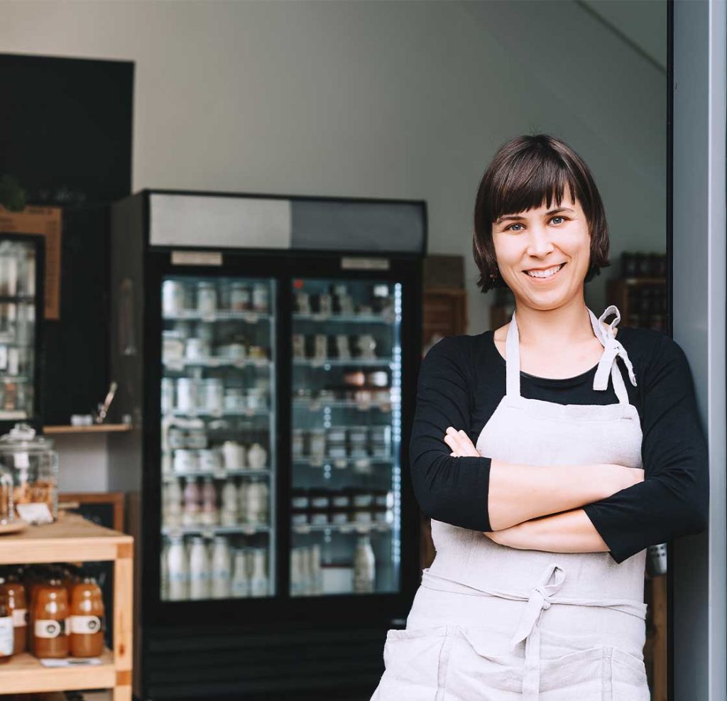 A local independent shop owner leans against her shop door. 